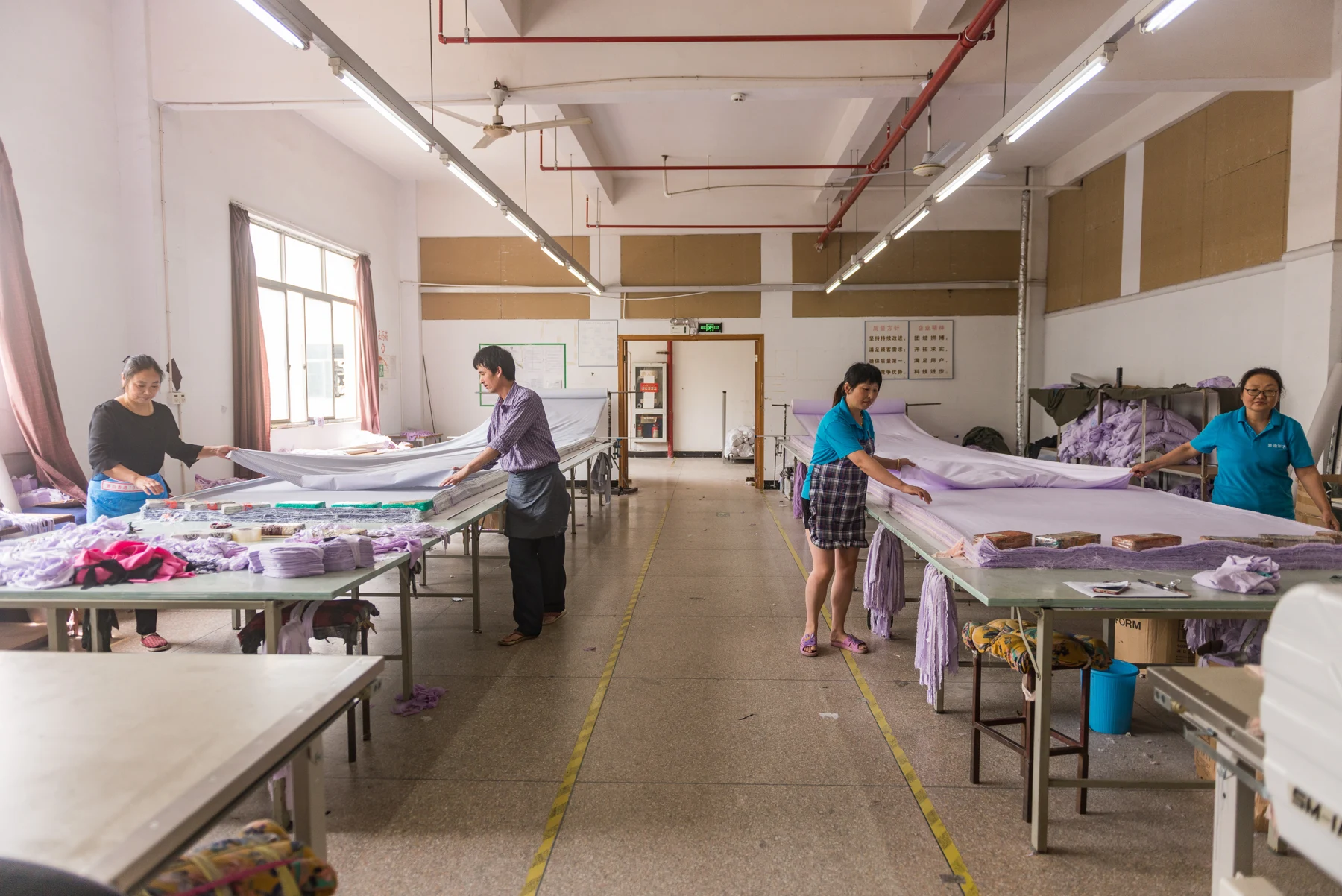 Workers spreading light purple fabric on cutting tables