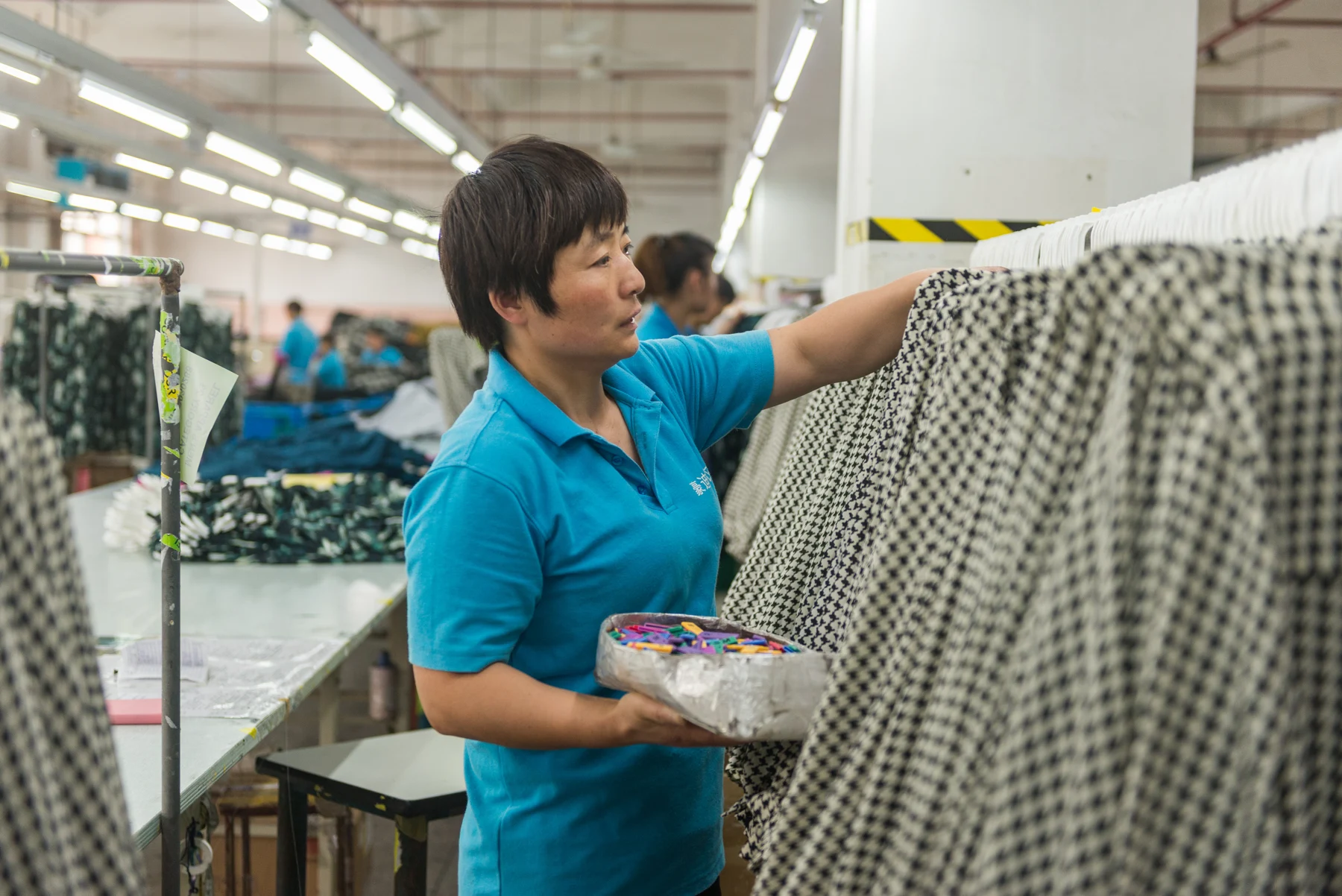 Worker checking patterned garments on a factory clothing rail