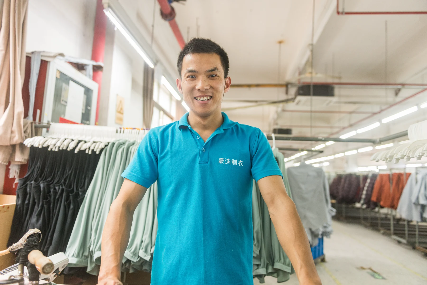 Garment worker at a pressing station beside clothing rails